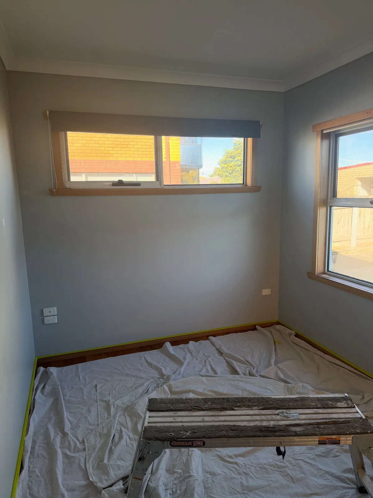 The bedroom before the repaint: dark grey-blue walls, drop sheets on the floor